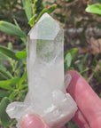 Video shows a clear quartz natural cluster with a large main point. It measures H 10cm W 6cm D 4cm