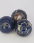 Image show three Sodalite polished spheres deep blue in colour with white, grey and brownish inclusions.