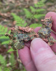 Video shows a native copper specimen. Green and copper in colour and freeform in shape. 