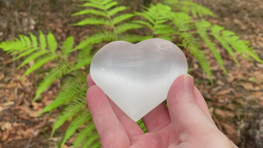 Video shows a selenite crystal polished into a heart shape, white in colour with a shiny lustre. 