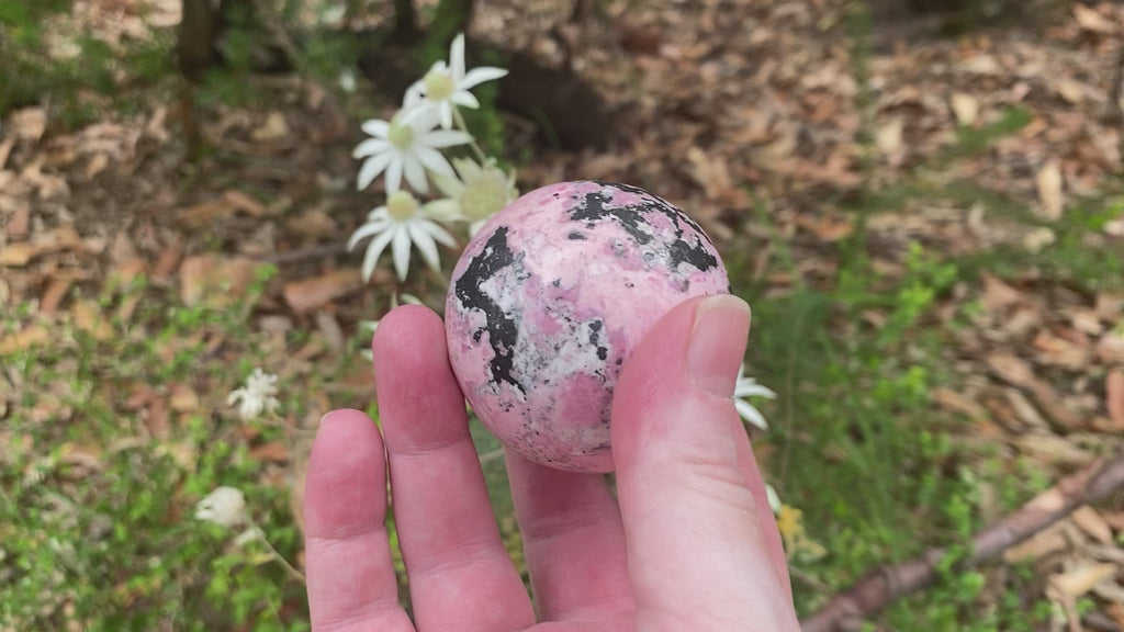 Video shows a Peruvian Rhodonite sphere. Pale pink, black and white in colour, the colours form intricate patterns on the surface of the sphere. 