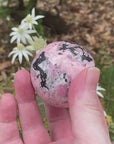 Video shows a Peruvian Rhodonite sphere. Pale pink, black and white in colour, the colours form intricate patterns on the surface of the sphere. 