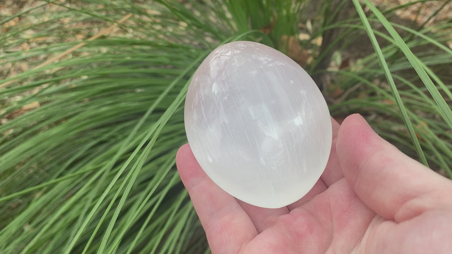 the video shows an oval shaped, polished selenite palm stone, white in colour with a shiny lustre. 