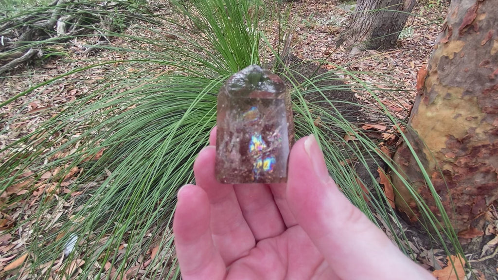 video shows a polished smokey quartz polished generator, it has rainbow inclusions and is a mid grey/brown colour. 