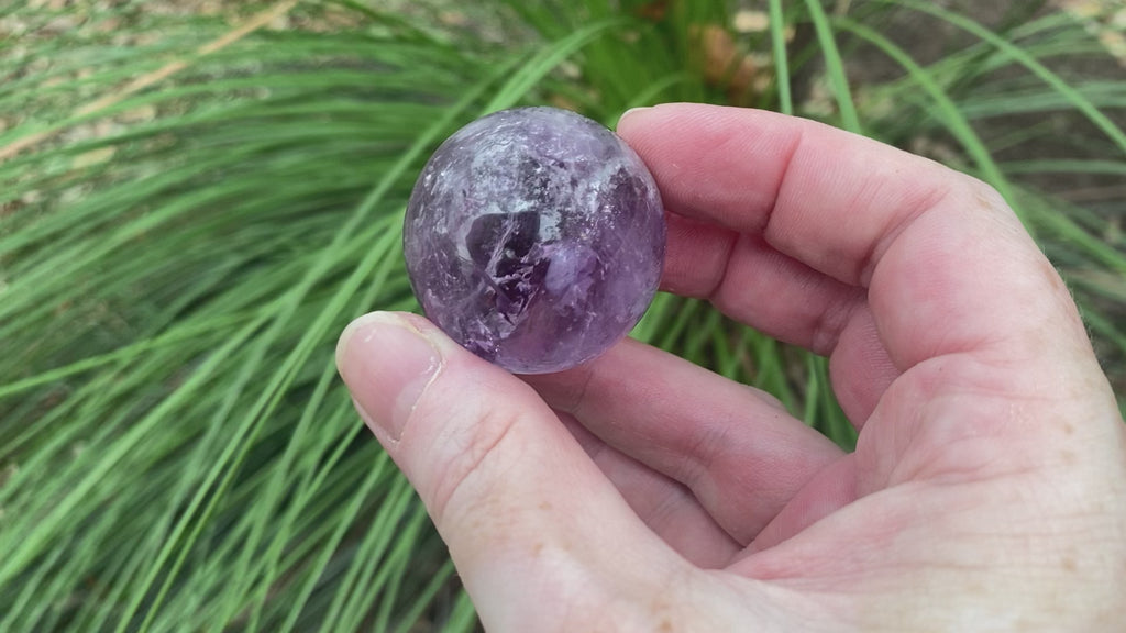 video shows an amethyst sphere, purple in colour and including lots of inclusions. 