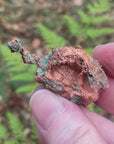 Video shows a native copper specimen. Green and copper in colour and freeform in shape. 