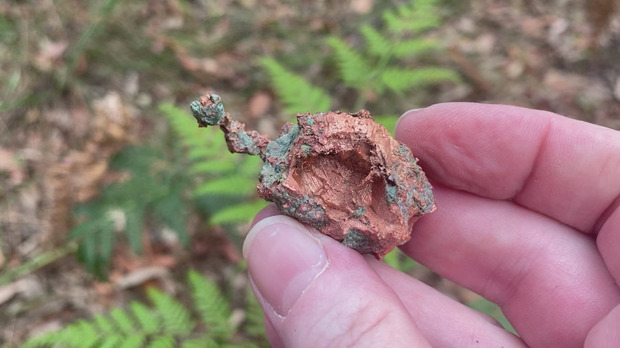 Video shows a native copper specimen. Green and copper in colour and freeform in shape. 