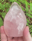 Video shows a polished rose quartz crystal in the shape of a flame. H 10 cm W 6.5cm D 6.5cm