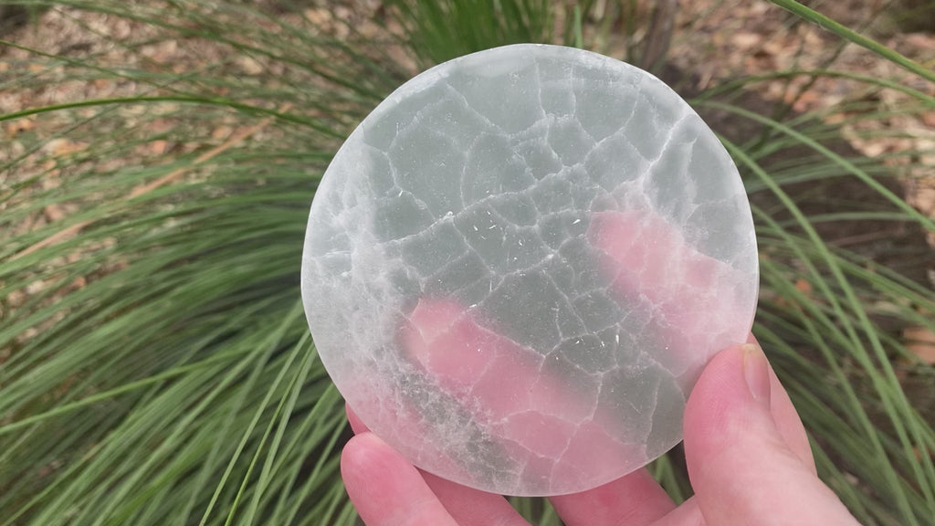 Video shows a selenite charging disc which is 15cm in diameter and 2cm thick. It is white in colour but also translucent. 