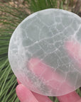 Video shows a selenite charging disc which is 15cm in diameter and 2cm thick. It is white in colour but also translucent. 