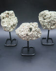 Image shows three pyrite clusters that have been attached to a black metal stand. 