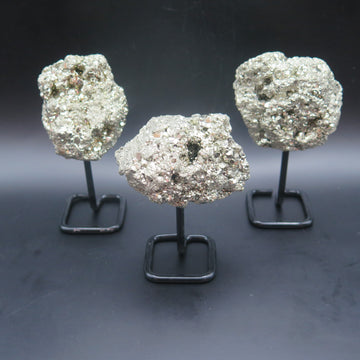 Image shows three pyrite clusters that have been attached to a black metal stand. 