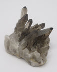 Image shows a smokey quartz cluster with very little matrix. It is blackish to dark grey in colour with translucent crystals. 