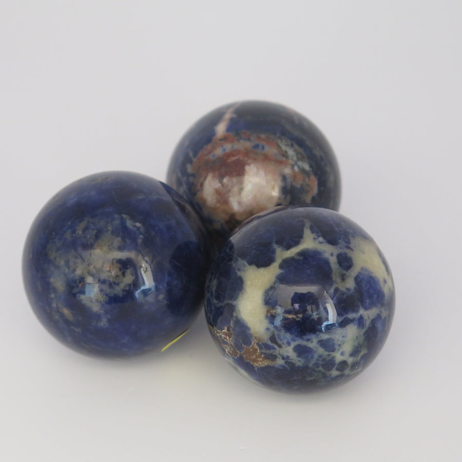 Image show three Sodalite polished spheres deep blue in colour with white, grey and brownish inclusions. 